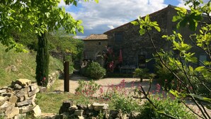 A stone building with a tiled roof, surrounded by a garden with flowering plants and a stone wall. - South Ardèche in Balazuc, listed site, Les Faysses self-catering gîte with charm and character (Balazuc)