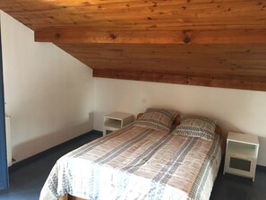 Une chambre avec un plafond en bois, un lit avec une literie à motifs, deux tables de chevet et une petite table de nuit.