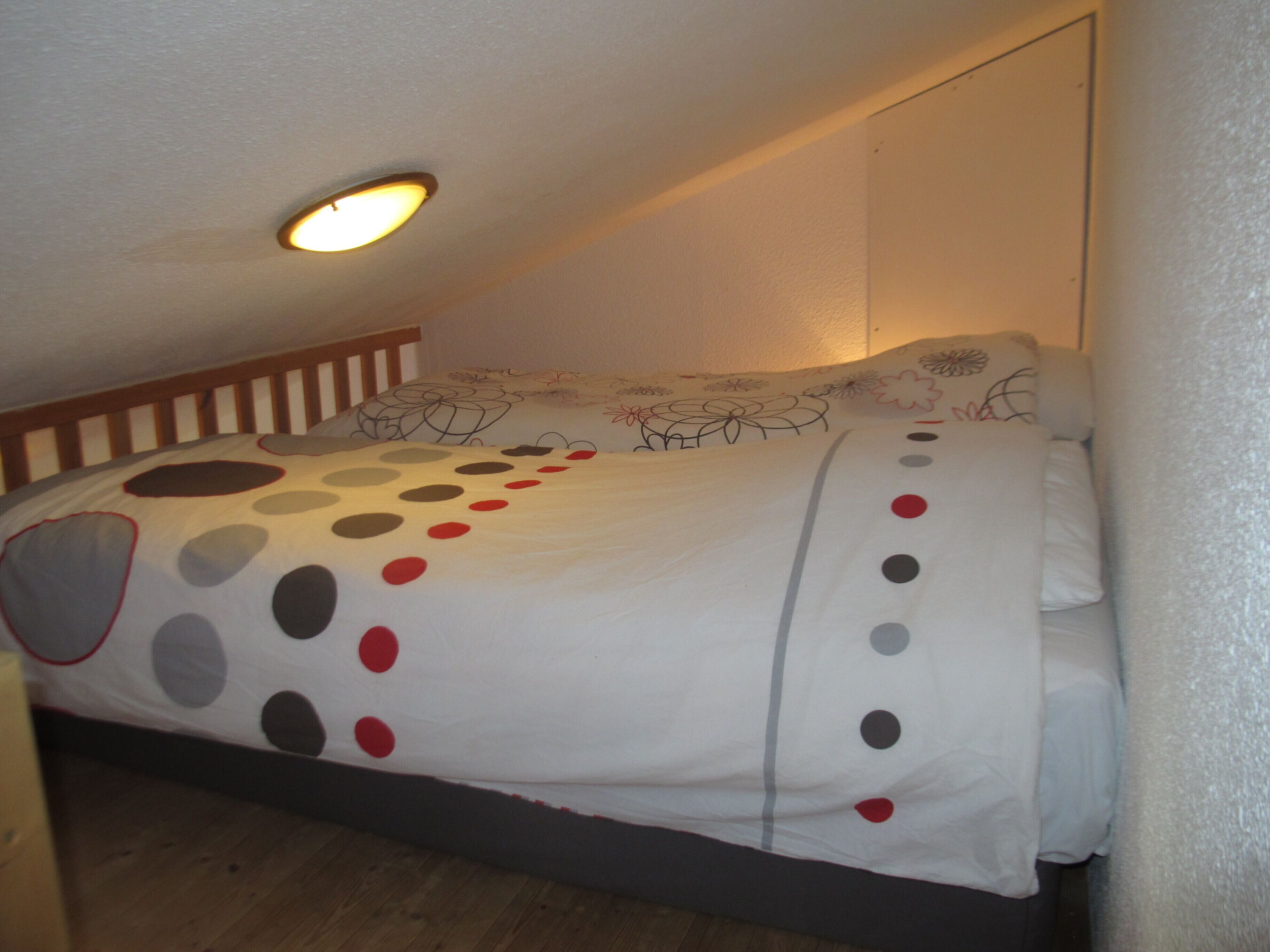 Een slaapkamer met een bed, houten hoofdeinde en een plafondlamp.
