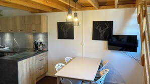 A modern kitchen with wooden beams, a dining table, chairs, and artwork on the wall. - Cozy & Elegant Apartment in Val Thorens, Ski-in/Ski-out, south-facing view, 36m2 (Les Belleville)