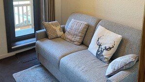 A living room with a grey sofa, two patterned pillows, a framed picture of a mountain, and a sliding glass door. - Cozy & Elegant Apartment in Val Thorens, Ski-in/Ski-out, south-facing view, 36m2 (Les Belleville)