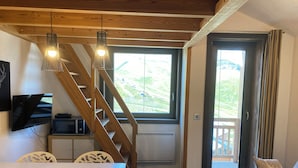 A cozy living room with a wooden staircase, a TV, a table with chairs, and a sofa with cushions. - Cozy & Elegant Apartment in Val Thorens, Ski-in/Ski-out, south-facing view, 36m2 (Les Belleville)