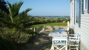 A wooden deck with a table and chairs, overlooking a scenic view of a body of water and distant buildings. - The terraces of the bay 'between land and sea' (Plounévez-Lochrist)