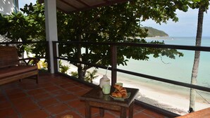 Un balcón con una mesa, un banco y vista a la playa y al océano.