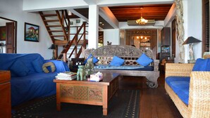 Una sala con un sofá azul, un sofá de mimbre, una mesa de centro de madera y una escalera.