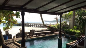 Un área de piscina con terraza de madera, sillas de descanso y vista a la playa y al océano.