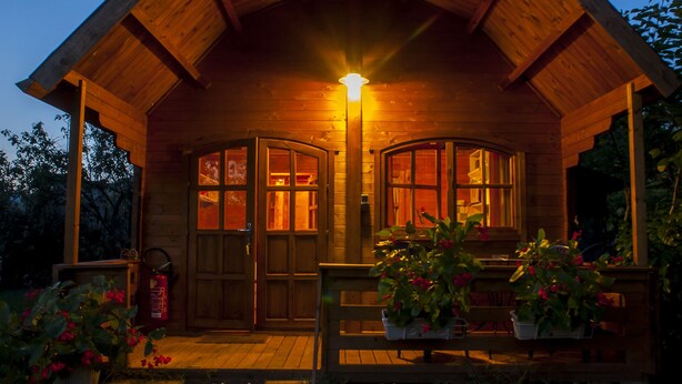 Eine Holzhütte mit Veranda, zwei Glasüren und einer beleuchteten Lampe.