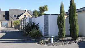 Une maison moderne avec une façade en pierre, une allée d’accès fermée par un portail et un jardin bien entretenu agrémenté de cyprès.