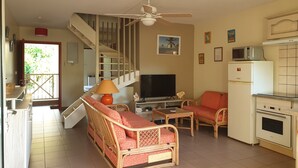 Una sala de estar con sofá, televisión, mesa de comedor y área de cocina con refrigerador y microondas.
