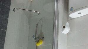 Eine Dusche mit Glastür, einer Handbrause und einem gelben Schwamm.