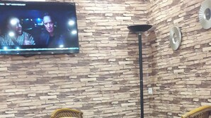 Ein Zimmer mit einer Steinwand, einem daran befestigten Flachbildfernseher und einem Tisch mit vier gelben Korbstühlen.