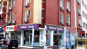 Un edificio rojo con varias ventanas y balcones, que incluye escaparates para 'Bulbul Optik' y 'Aveda'.