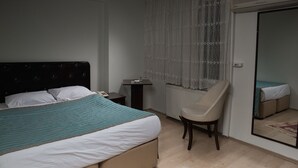 Un dormitorio con una cama, una silla, una mesita de noche, una mesa y una ventana con cortinas.
