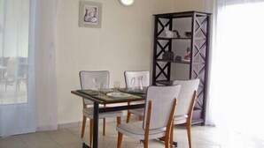 A dining area with a table set for two, two chairs, a wall-mounted light, and a decorative cabinet. - Vacation Rental in Cambo-Les-Bains: 2-room, air-conditioned, fully equipped—panoramic view. (Cambo-Les-Bains)