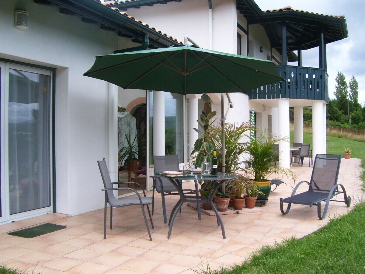 Une terrasse extérieure avec une table, des chaises et un grand parasol.