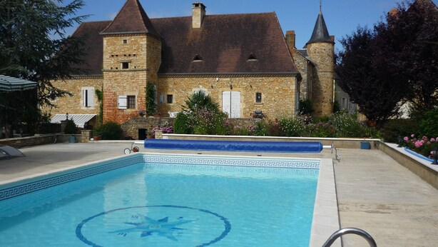 Une piscine ornée d’un motif en forme d’étoile, entourée d’un bâtiment en pierre doté d’une tourelle et d’un patio couvert.