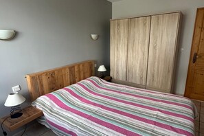Un dormitorio con cabecera de madera, colcha a rayas, armario de madera y lámparas de noche.