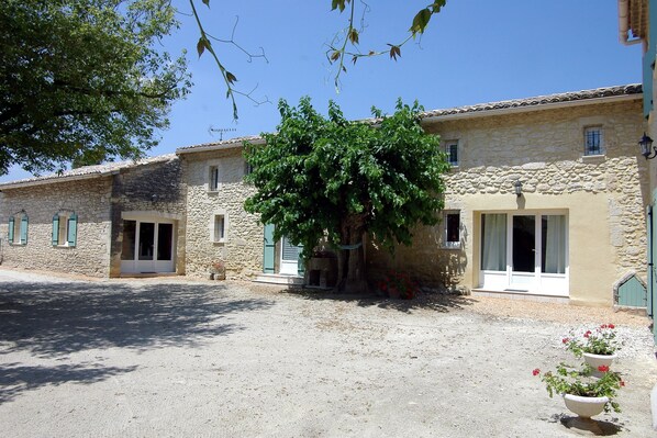 A stone building with a tree in front, a gravel courtyard, and a small flower pot. - Uzès superb, comfortable gîte with swimming pool 700m from town center:  (Uzès)