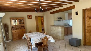 Un coin repas avec une table et des chaises en bois, un buffet avec des portes en verre, et une cuisine en arrière-plan.
