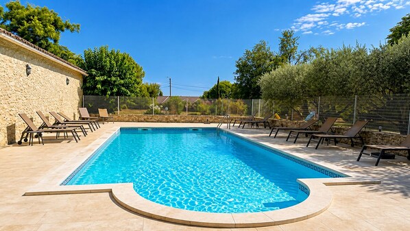 Une piscine rectangulaire dont le bord est recouvert de carreaux, entourée de chaises longues et d’un mur en pierre.