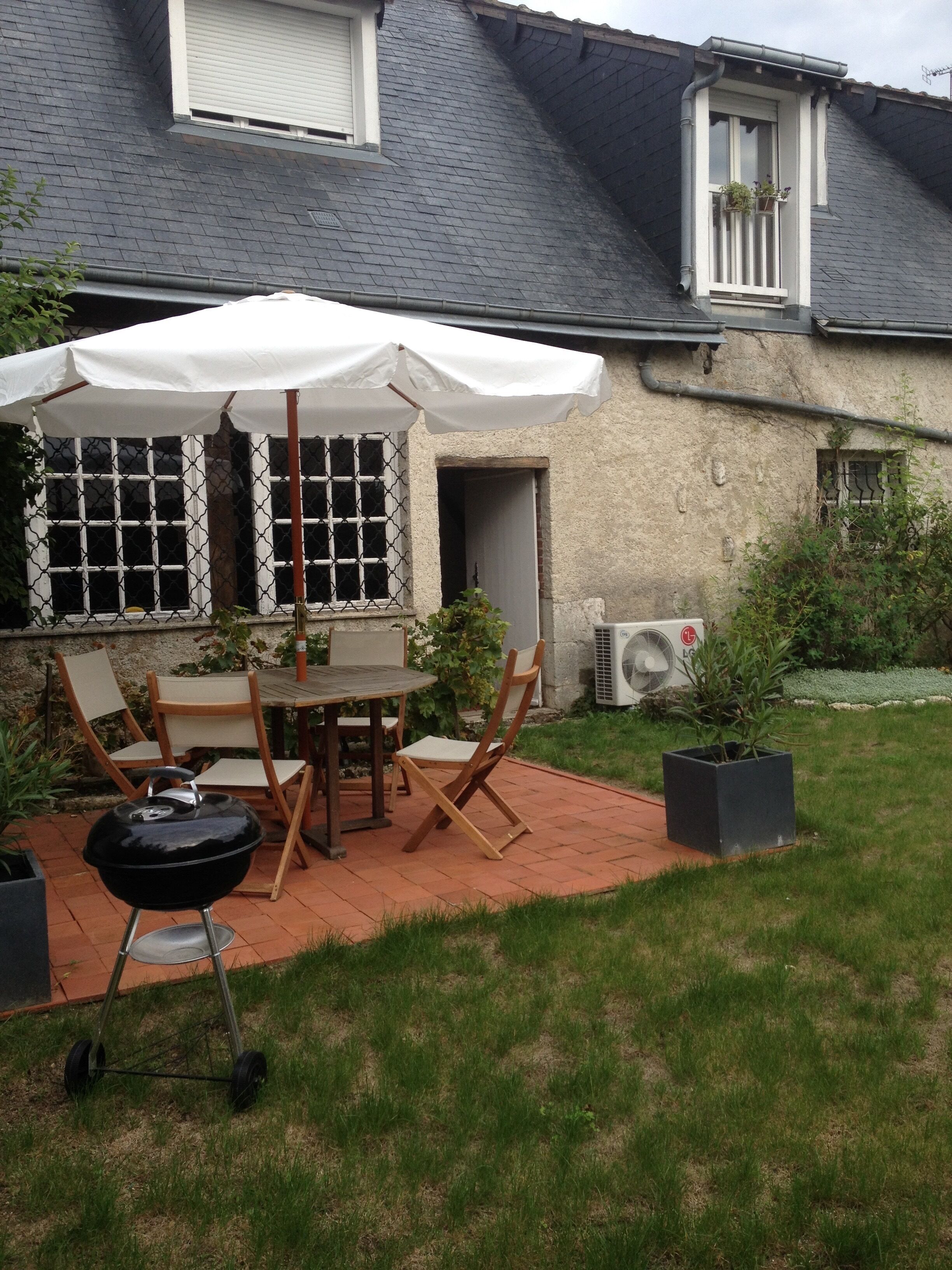 A patio with a table and chairs, a barbecue grill, and a white umbrella.