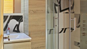 Een moderne badkamer met een douchecabine van glas, een witte wastafel en een houten opbergmeubel.