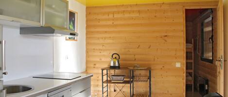 Une cuisine avec des murs en bois, une cuisinière en acier inoxydable et une étagère en métal où sont rangés les ustensiles de cuisine.
