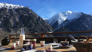 Una mesa servida con platos, tazas y una botella, con vistas a montañas nevadas.