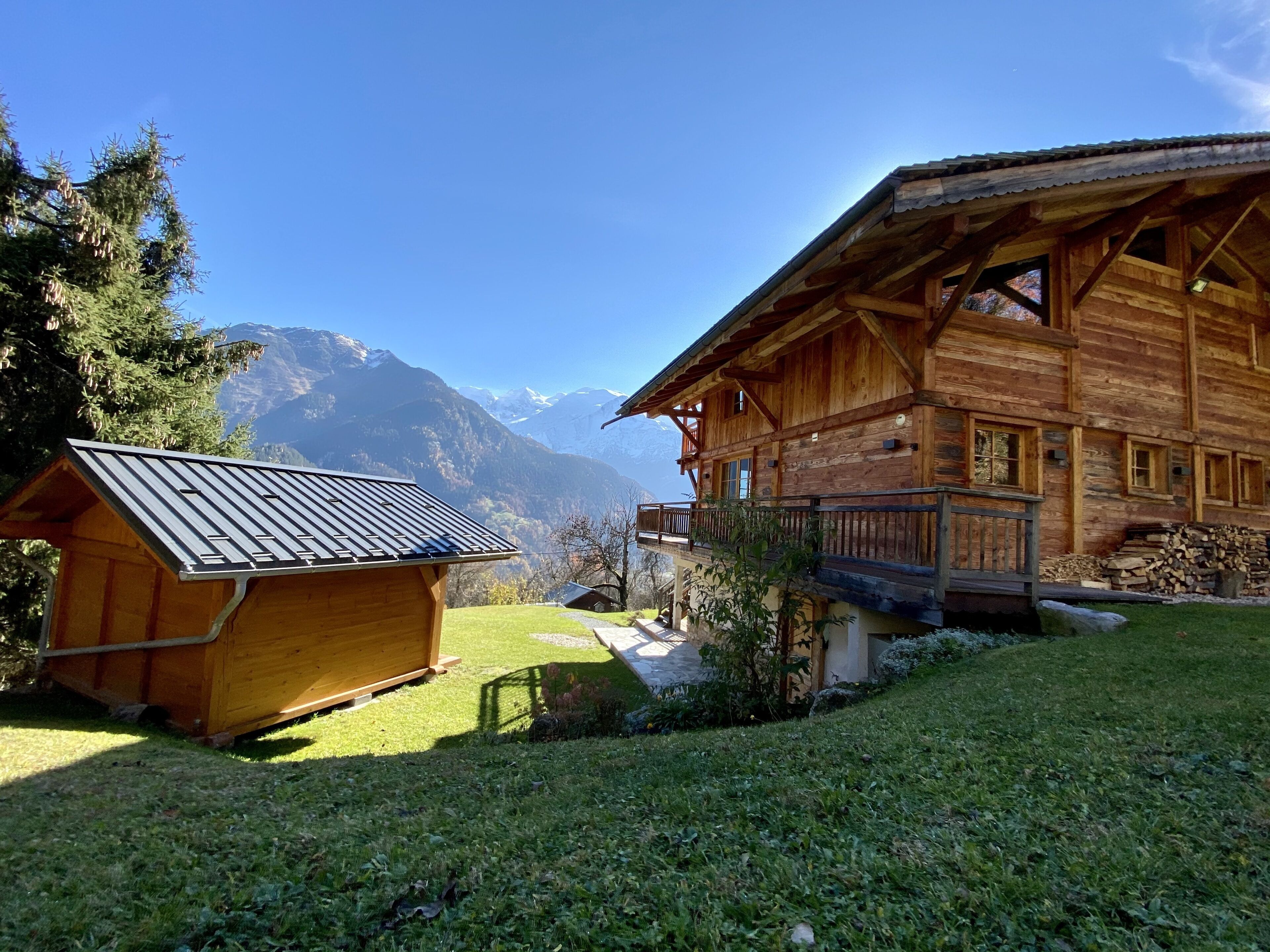 Un chalet en bois doté d’un balcon, d’un petit abri de jardin et surplombant un paysage montagneux.