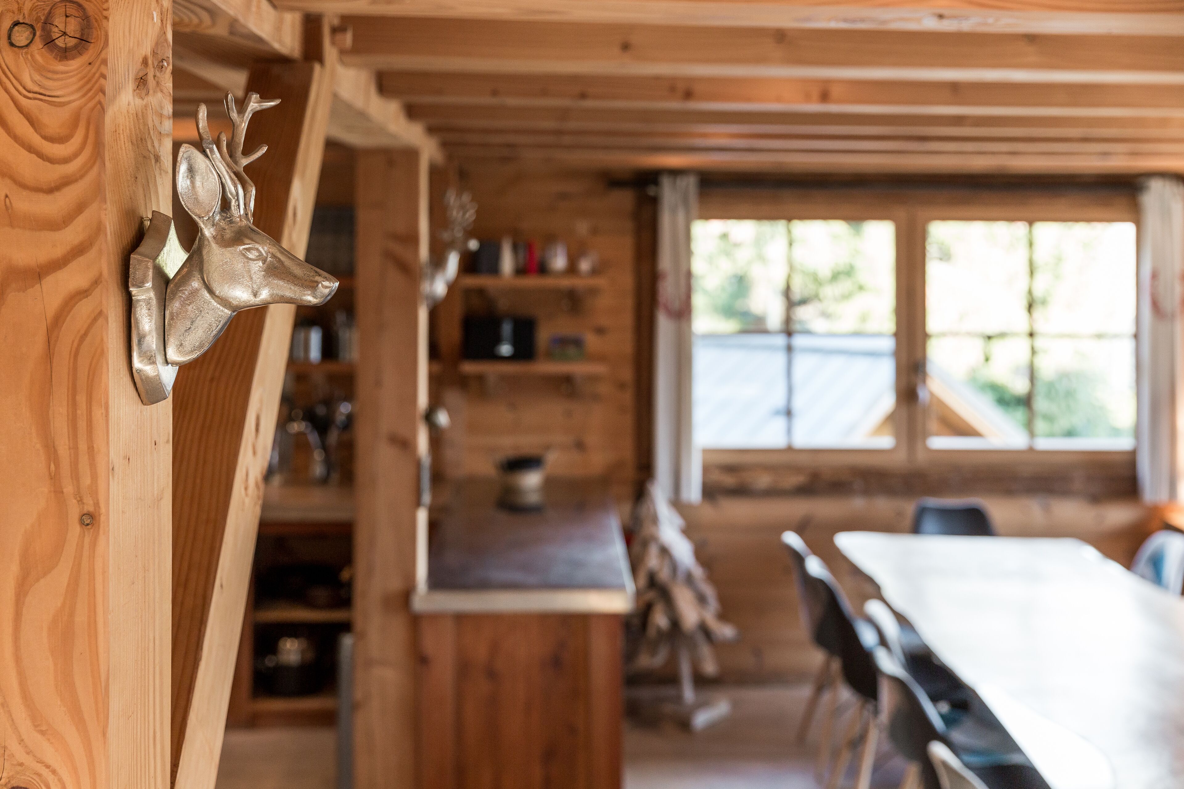 Een houten interieur met een eethoek, planken met diverse spullen en een raam met uitzicht op groen.