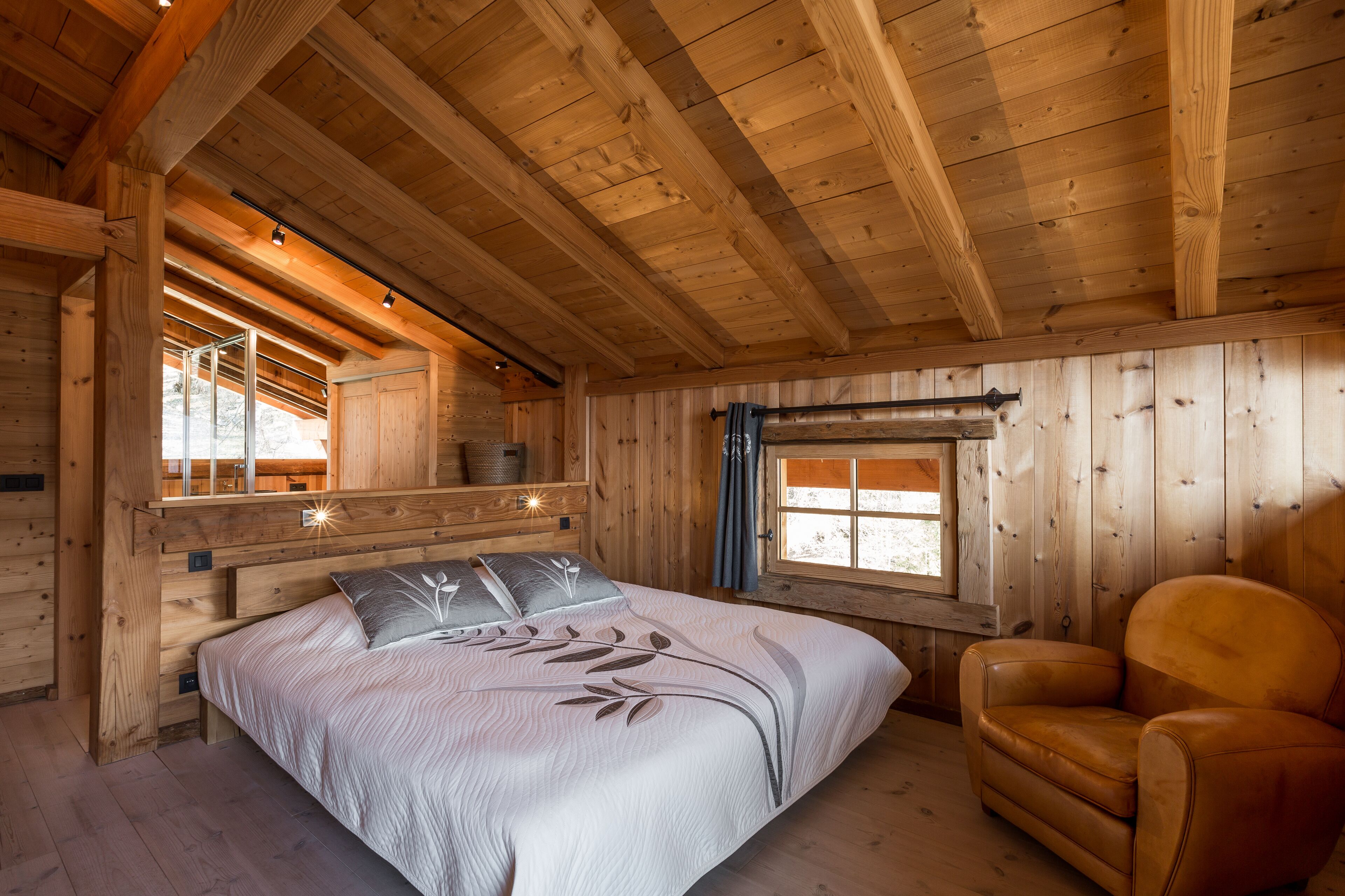 A wooden cabin room with a bed, a chair, and a window.