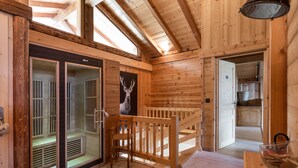 Interior de una cabaña de madera con un vidrio que da a un balcón, un banco de madera y una mesa de comedor con un cuenco de vidrio.