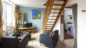 Uma sala de estar com dois sofás, uma estante de livros, uma televisão e uma escada que dá para uma área de serviço.