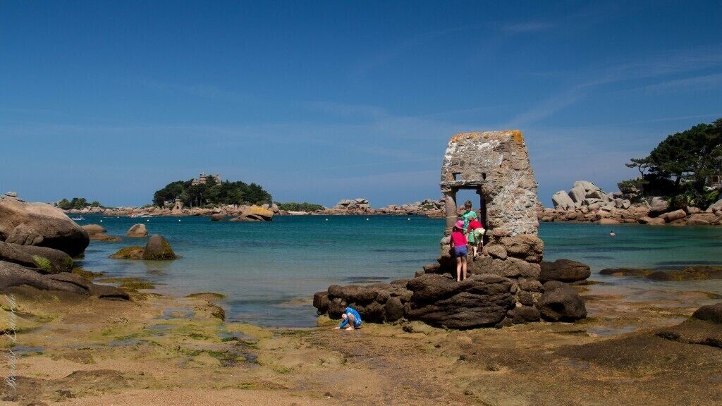 A coastal scene with a stone structure, clear blue water, and rocky terrain.