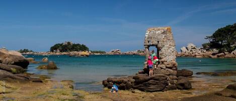 A coastal scene with a stone structure, clear blue water, and rocky terrain.