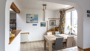 Uma área de refeições com uma mesa posta para quatro pessoas, um banco e vista para a cozinha através de um arco.