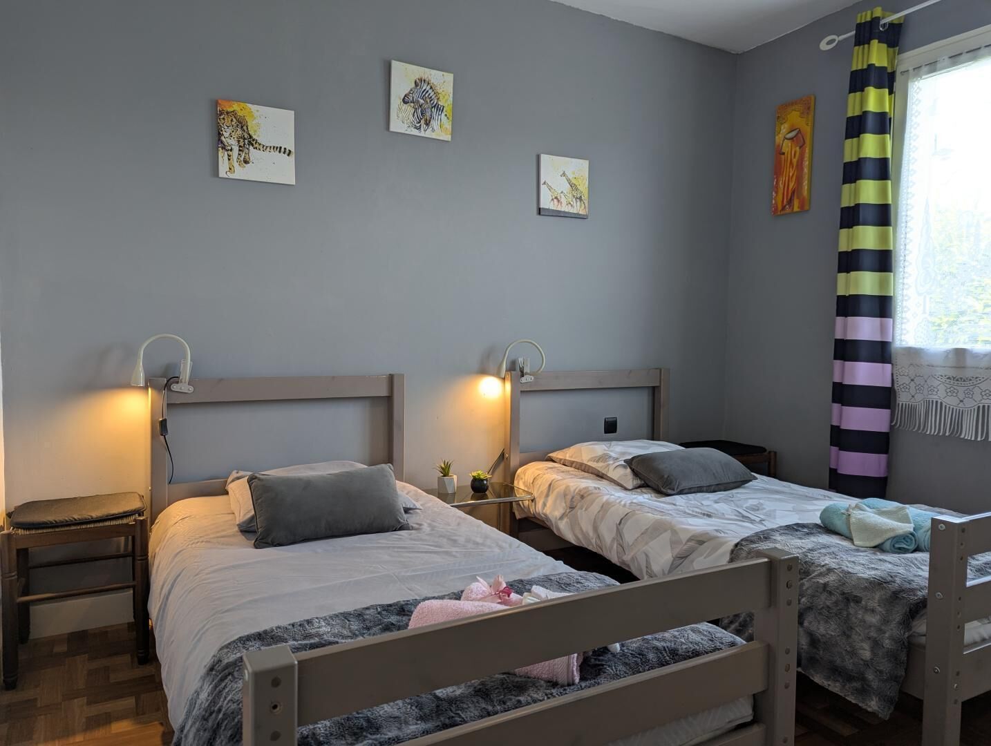 Une chambre avec deux lits, des tables de chevet, des œuvres d’art murales et une fenêtre avec des rideaux.