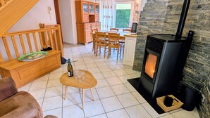 A cozy living room with a fireplace, wooden furniture, and a kitchen area in the background. - Renovated stone house, classified 3 stars between La Bresse and Gérardmer (Basse-Sur-Le-Rupt)