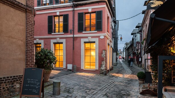 Un carrer empedrat estret amb un edifici vermell, amb grans finestres i persianes.