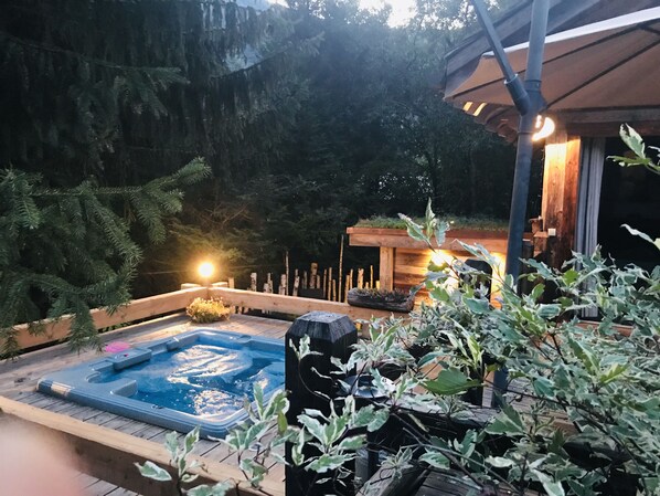 Een hottub omgeven door houten terrassen, een houten hek en een pergola met verlichting.