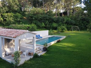 A modern outdoor pool area with a patio, lounge chairs, and a swing set.