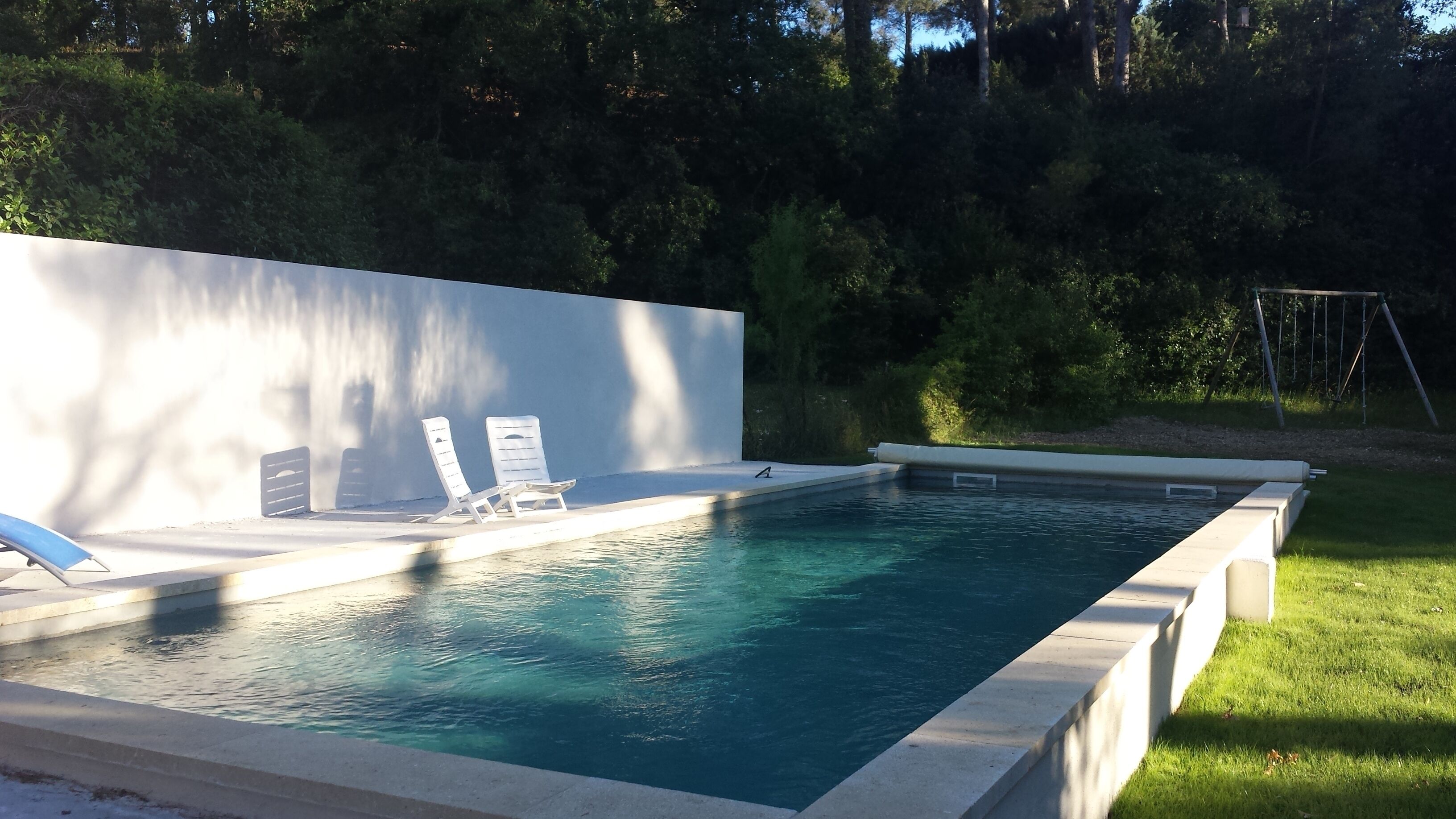Une piscine rectangulaire avec deux chaises longues et un mur blanc.
