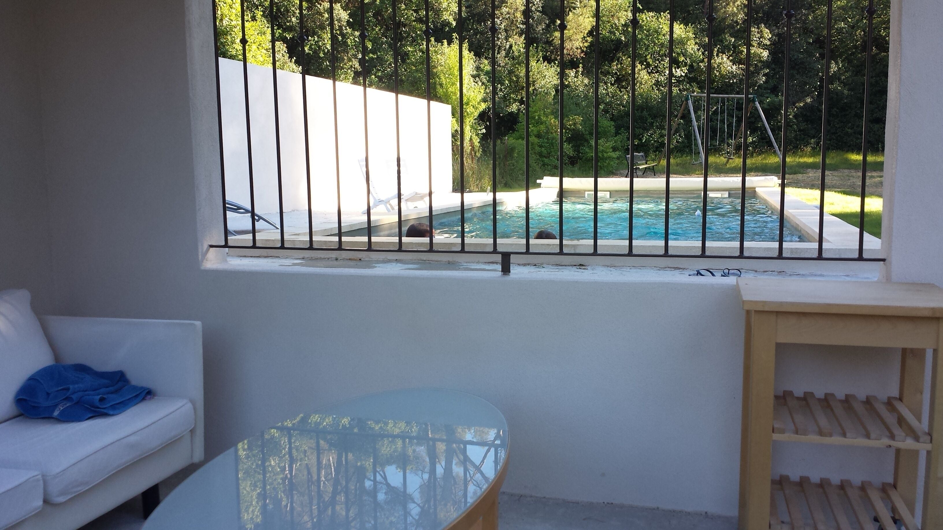 Un balcó amb vista a una piscina, un sofà blanc i una taula de vidre.