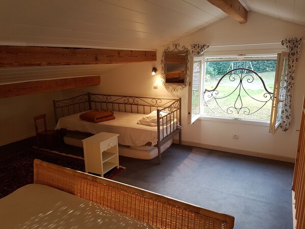 A cozy bedroom with a bunk bed, a small white cabinet, a wicker chair, and a window with a decorative iron grille.