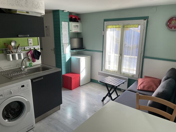 Una cocina compacta equipada con lavadora, un refrigerador pequeño y una zona de comedor con mesa y sillas.