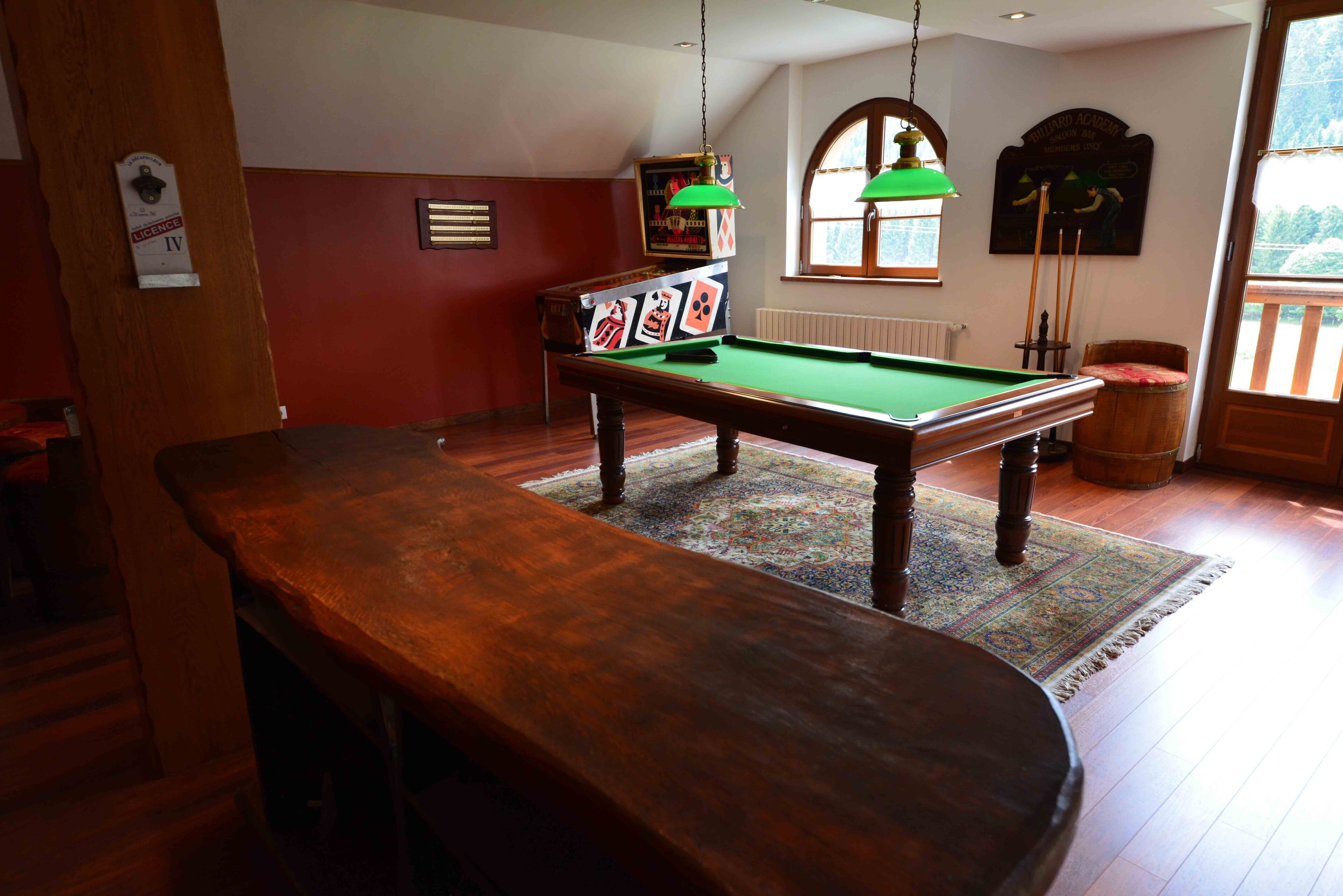 Una mesa de billar con superficie de fieltro verde, una mesa de pool de madera y una alfombra estampada.