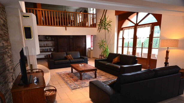 Ein geräumiges Wohnzimmer mit einer schwarzen Ledersofa, einem Holztisch und einem Bücherregal. Ein großes Fenster lässt natürliches Licht herein.