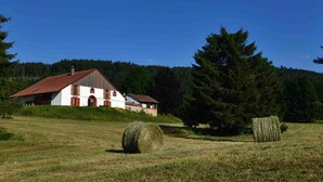 Ein ländliches Bauernhaus mit rotem Dach, umgeben von Heuballen und einer großen Kiefer.