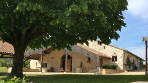 Un edificio de piedra con techo de tejas, ventanas arqueadas y un patio cubierto.