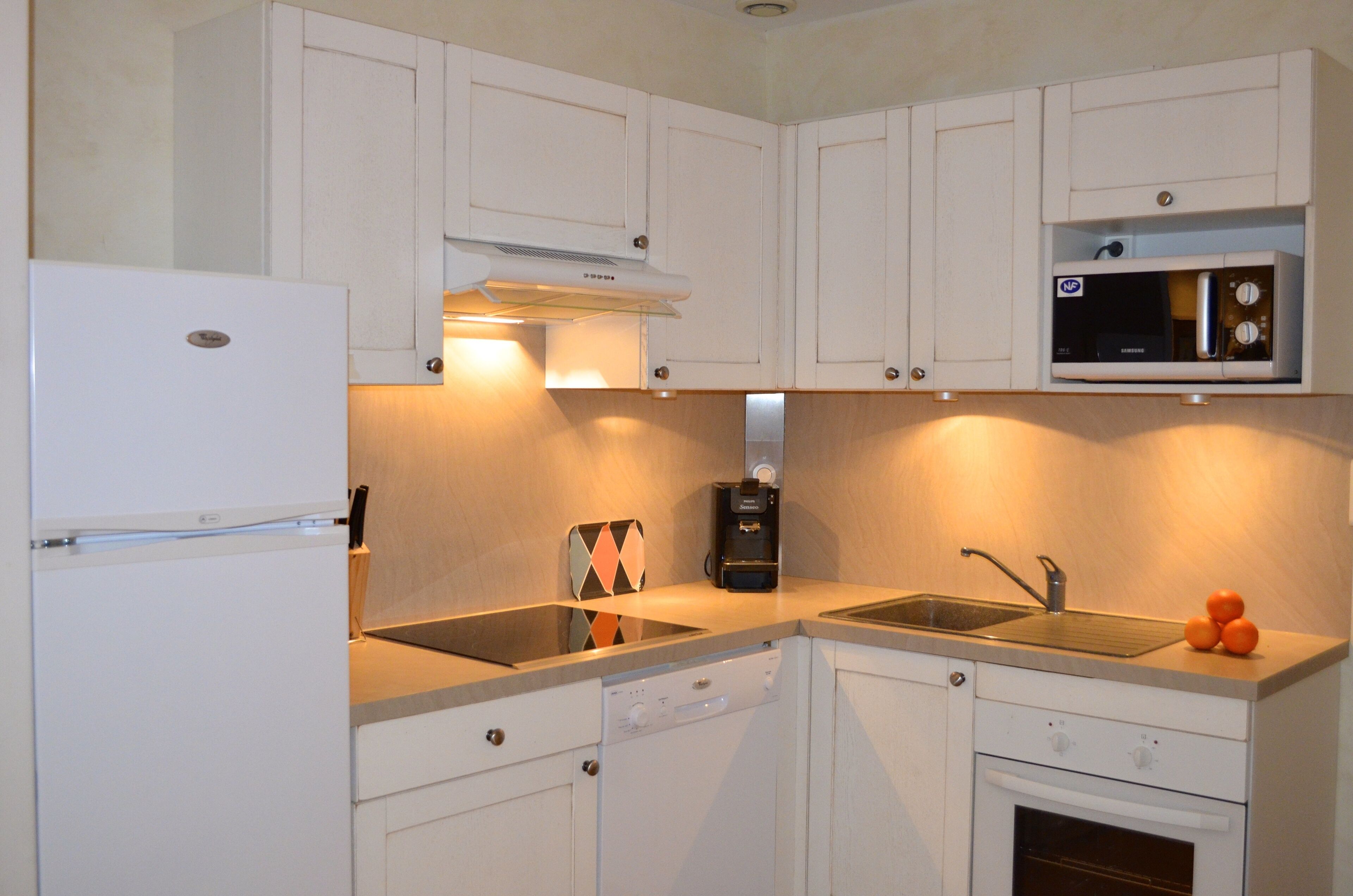A compact kitchen with white cabinets, a built-in microwave, a dishwasher, and a sink.